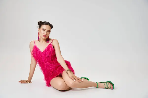 Confident woman in fashionable pink outfit sitting boldly, touching her knee, on grey background — Stock Photo