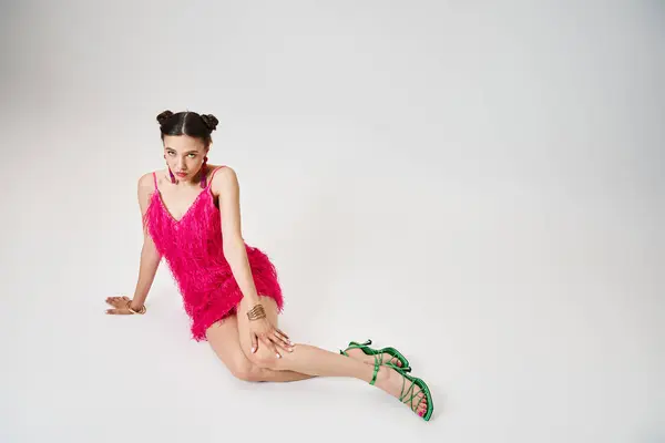 Radiant lady in pink dress touching her knee, sitting and looking at camera on grey background — Stock Photo