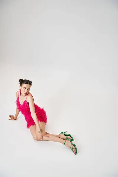 Hübsche Frau im rosafarbenen Kleid, die ihr Knie berührt, sitzt und wegschaut auf grauem Hintergrund — Stockfoto