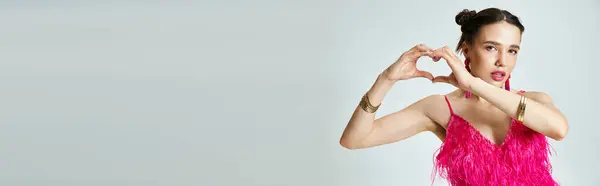 Donna bruna con naso traforato che indossa un abito di piume rosa che mostra un cuore di mano alla macchina fotografica, banner — Foto stock