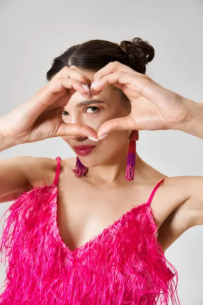 Sexy joyful brunette woman wearing pink feather dress showing a hand heart to camera — Stock Photo