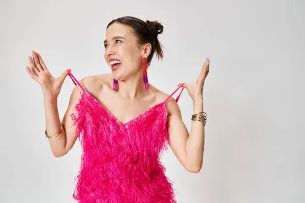 Laughing brunette woman in pink outfit looking away, holding straps of her dress on grey background — Stock Photo