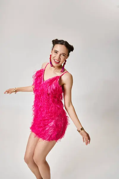 Femme heureuse en tenue rose chic et bijoux fantaisie dansant joyeusement sur fond gris — Photo de stock