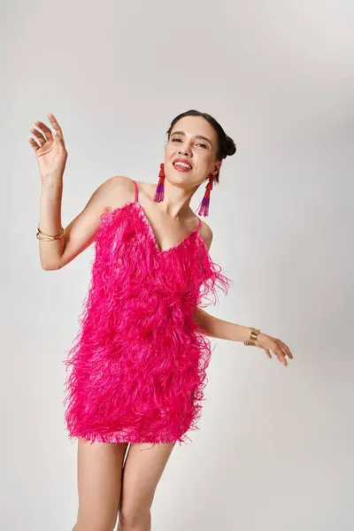 Jolie femme en robe rose tendance et bijoux fantaisie dansant joyeusement sur fond gris — Photo de stock