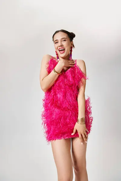 Веселая брюнетка в стильном розовом платье смеется жестом на сером фоне — стоковое фото