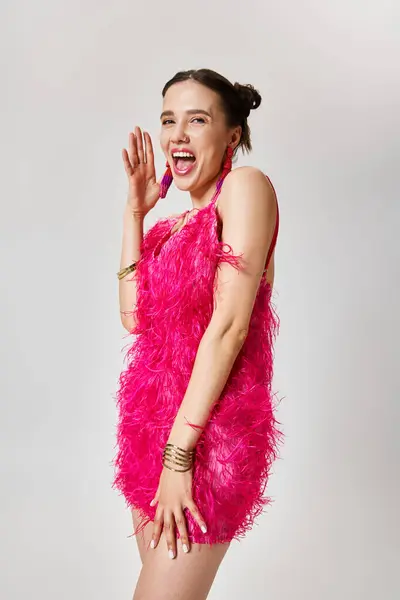 Mujer divertida en elegante vestido rosa se ríe, toca su mejilla, sobre fondo gris - foto de stock