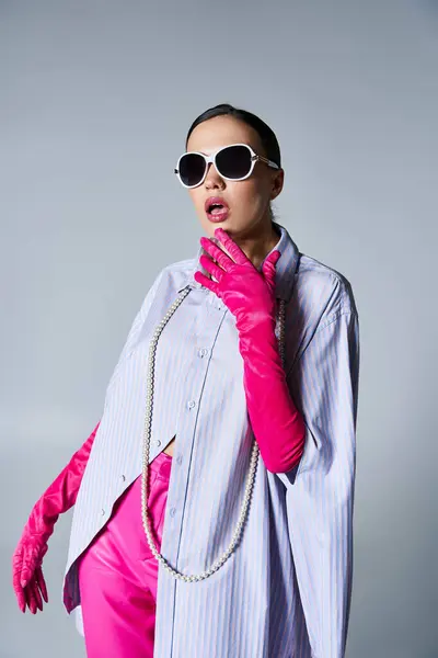 Fashionable brunette in pink trousers and violet shirt, wearing stylish sunglasses, touches her chin — Stock Photo