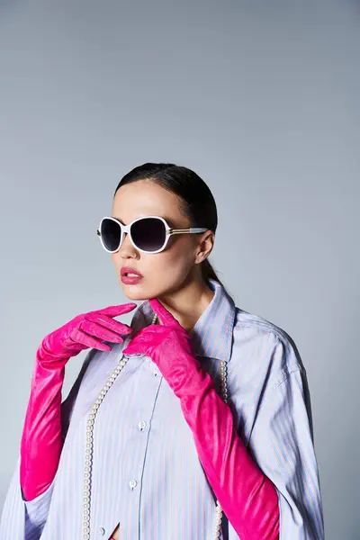 Schöne brünette Frau in trendiger Kleidung und Sonnenbrille, die im Studio ihr Kinn berührt — Stockfoto