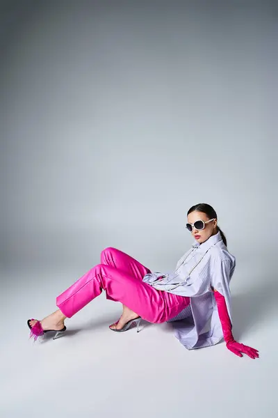 Mulher elegante em luvas rosa, calças de couro e óculos de sol chiques deitado sobre fundo cinza — Stock Photo