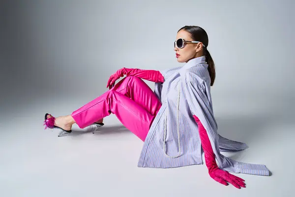 Vue arrière de la femme en gants roses, pantalon en cuir et lunettes de soleil assis sur fond gris — Photo de stock