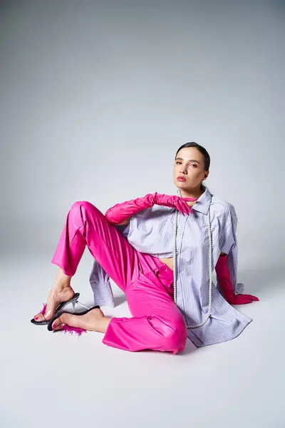 Elegante morena con guantes y pantalones de cuero rosa sentada y agarrada de la mano cerca de la cara - foto de stock