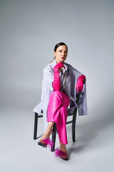 Chica morena confiada con guantes de color rosa, zapatos de plumas y pantalones elegantes, sentado en la silla - foto de stock