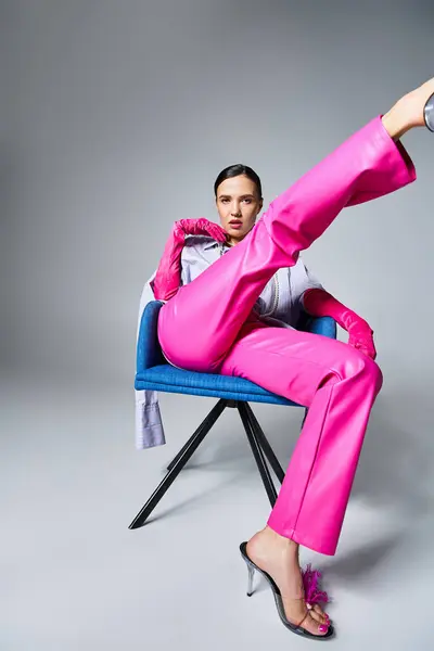 Mujer morena confiada en pantalones y zapatos rosas de moda, sentada y pateando su pierna - foto de stock