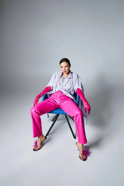 Шикарная брюнетка в перчатках и розовых штанах сидит на стуле и уверенно смотрит в камеру. — стоковое фото