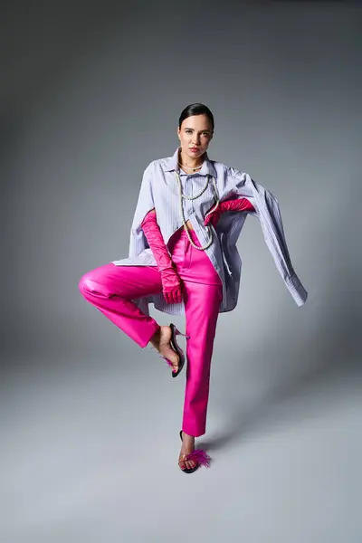 Brune à la mode portant des gants roses et un pantalon en cuir debout dans la pose de mode isolé — Photo de stock