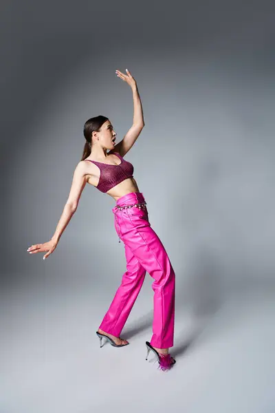 Full length photo of brunette woman in red top and pink pants making a step on grey background — Stock Photo