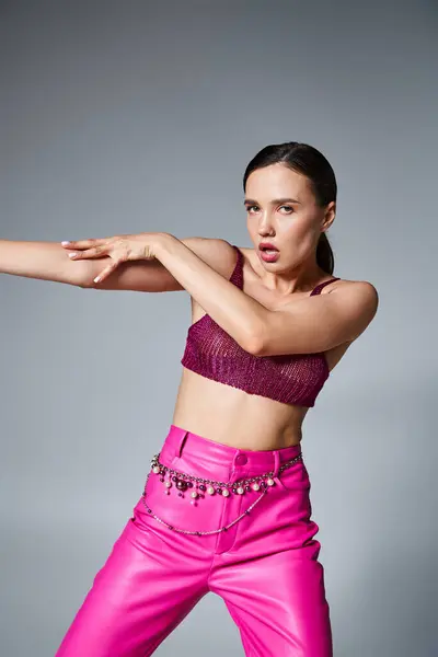 Morena mujer sexy confiada en la parte superior de burdeos de punto elegante y pantalones de color rosa tocando su mano - foto de stock