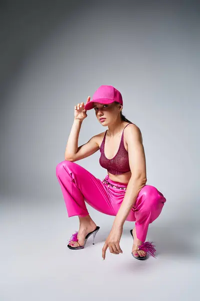 Fancy brunette woman in red top and pink trousers sitting and touching pink cap with one hand — Stock Photo