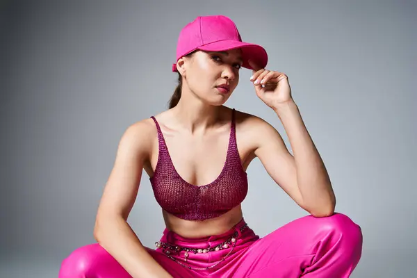 Sexy stylish woman in red top and pink trousers sitting and touching pink cap with one hand — Stock Photo