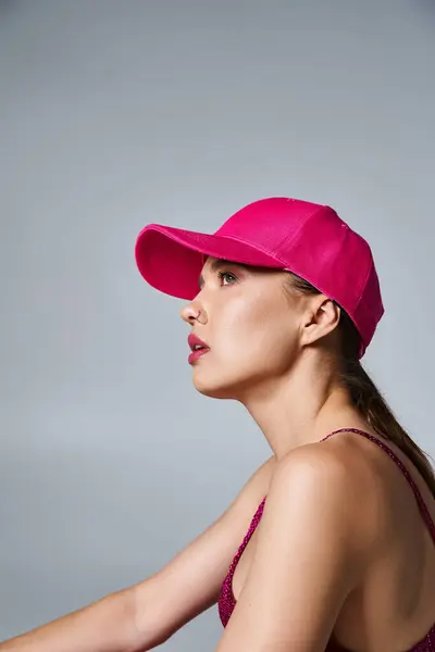 Vista lateral de la hermosa mujer morena en traje de moda y gorra rosa en el entorno del estudio - foto de stock