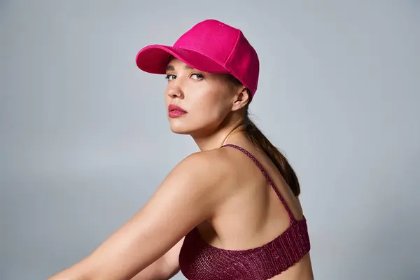 Вид сзади женщины в вязаном бордовом топе и розовой кепке, сидящей на сером фоне — стоковое фото