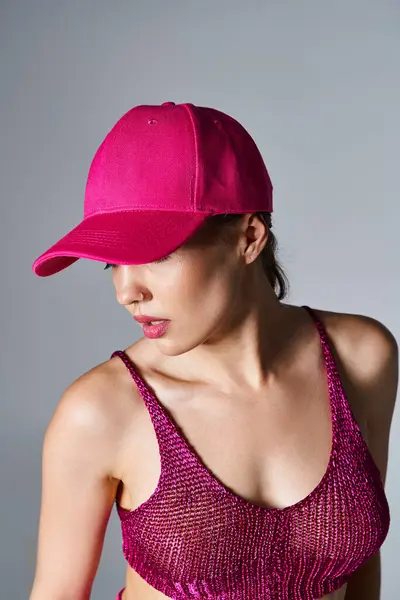 Брюнетка з пірсингом у стильному вбранні з червоною верхньою і рожевою шапочкою, дивиться в сторону на сірий — стокове фото