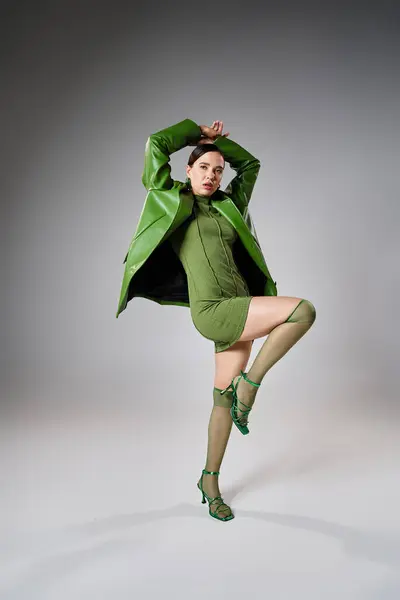 Modebewusste Brünette in total grünem Trendlook tanzt vor grauem Hintergrund im Studio-Setting — Stockfoto