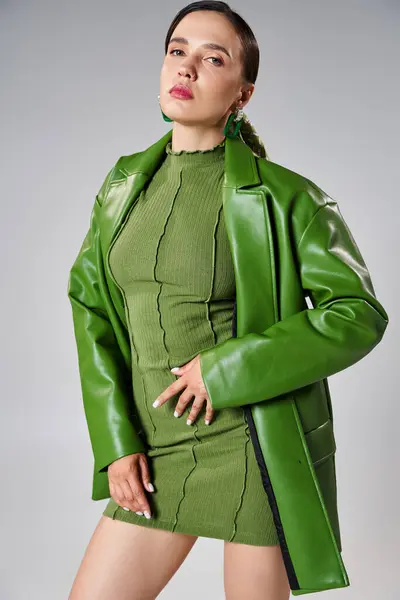 Sexy and confident brunette woman in total green trendy look touching her body in studio setting — Stock Photo