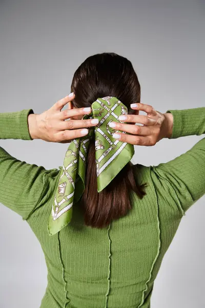 Rückansicht einer jungen brünetten Frau im grünen Outfit, die ihr lebendiges Kopftuch berührt — Stockfoto