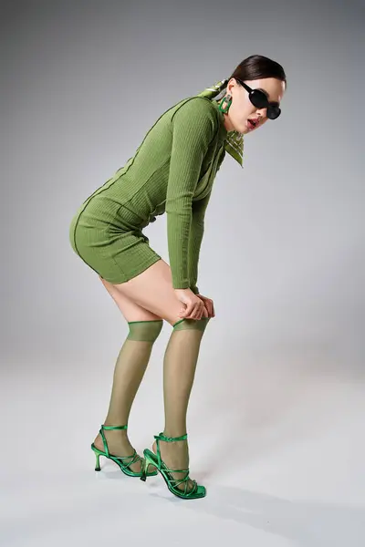 Donna di fantasia in mini abito verde e calzini al ginocchio, indossando occhiali neri e toccando il ginocchio — Foto stock