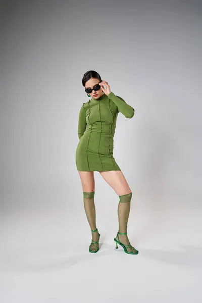 Femme sexy et élégante portant une tenue verte et touchant ses lunettes de soleil à la mode avec une main — Photo de stock