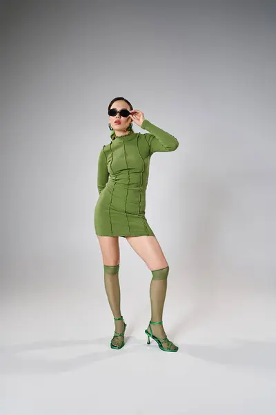 Ganztägiges Foto einer stilvollen Frau mit grünem Outfit und berührender Sonnenbrille mit einer Hand — Stockfoto