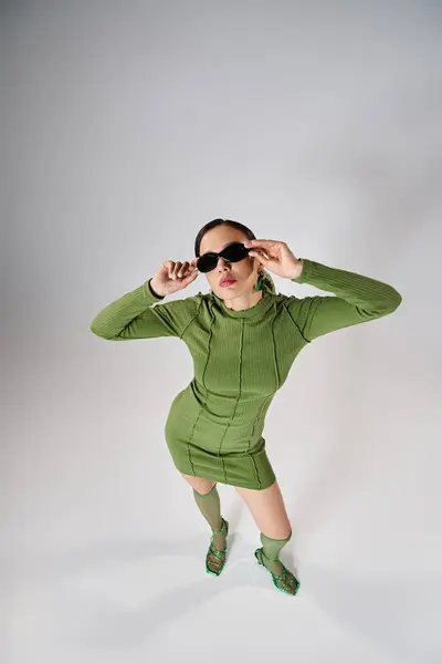 Vista superior de la mujer en mini vestido verde y calcetines de rodilla, tocando sus gafas con ambas manos - foto de stock
