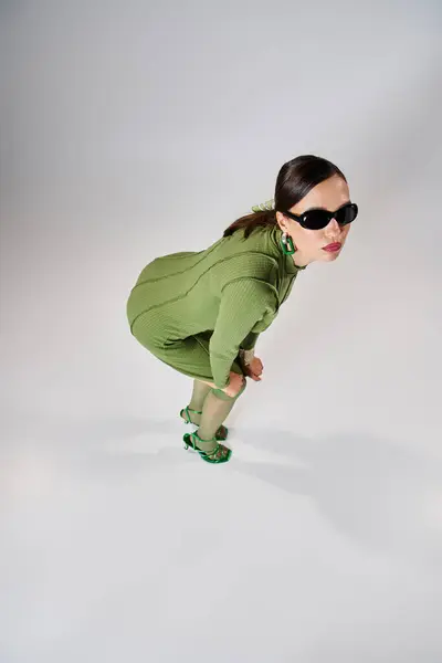 Vista dall'alto della donna in abito verde e occhiali da sole toccare le gambe con e guardando la fotocamera — Foto stock