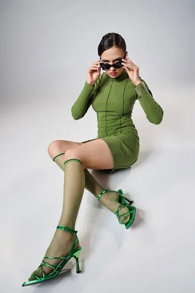 Sexy donna elegante indossa total look verde e toccare i suoi occhiali da sole sdraiato su sfondo grigio — Foto stock