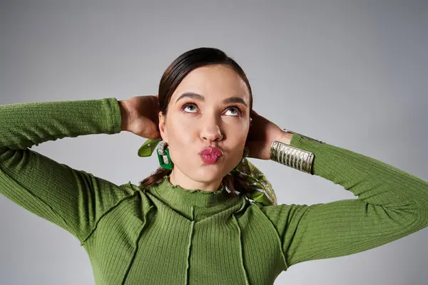 Divertito fantasia bruna donna in abito verde che soffia baci e guardando su sfondo grigio — Foto stock