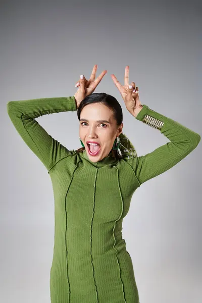 Mulher alegre em verde traje elegante sorrindo alegremente mostrando sinais de paz com as mãos — Fotografia de Stock