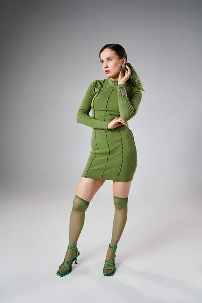 Femme brune en mini robe verte, chaussettes et chaussures de genou, porter des bijoux élégants, mains sur son corps — Photo de stock