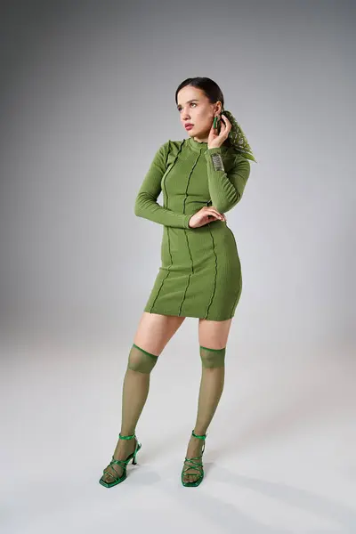 Mujer morena en mini vestido verde, calcetines y zapatos de rodilla, con joyas elegantes, manos en su cuerpo - foto de stock