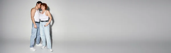 Appealing couple in blue jeans posing together lovingly on gray background, relationship, banner — Stock Photo