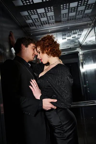 Tempting joyful boyfriend and girlfriend in elegant black attires hugging in elevator, sexy couple — Stock Photo