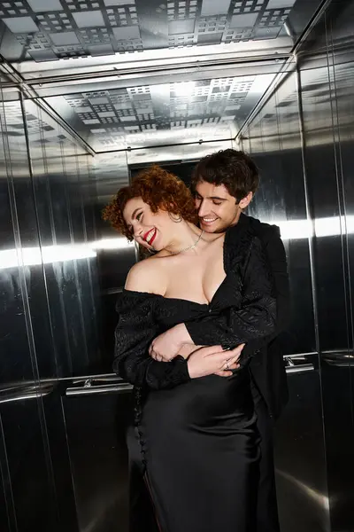 Allettante gioioso fidanzato e fidanzata in eleganti abiti neri abbracciati in ascensore, coppia sexy — Foto stock