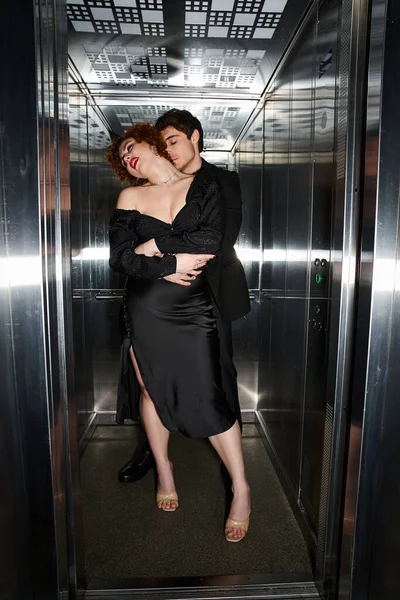 Enticing loving boyfriend and girlfriend in elegant black attires hugging in elevator, sexy couple — Stock Photo