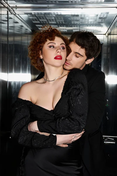 Sexy appealing couple in elegant black dress and suit hugging lovingly in elevator after date — Stock Photo