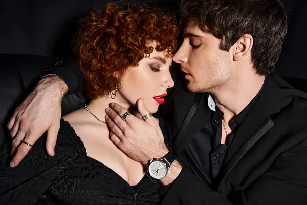 Engaging boyfriend and girlfriend in elegant clothes hugging lovingly on black sofa, sexy couple — Stock Photo