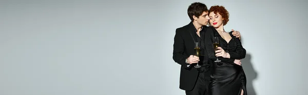 Hübsche Frau in schwarzem Kleid umarmt ihren hübschen Freund vor grauem Hintergrund, Champagner, Banner — Stockfoto