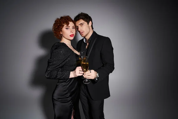 Sexy gut aussehendes Paar in schwarzer Kleidung, das sich umarmt und mit Champagner in der Hand in die Kamera blickt — Stockfoto