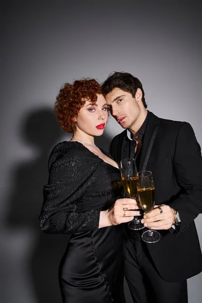 Sexy gut aussehendes Paar in schwarzer Kleidung, das sich umarmt und mit Champagner in der Hand in die Kamera blickt — Stockfoto