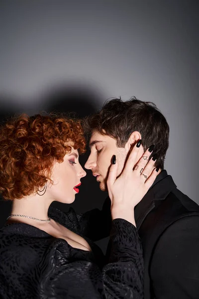 Atractivo sexy pareja en negro elegante trajes preparándose para besarse en gris telón de fondo - foto de stock