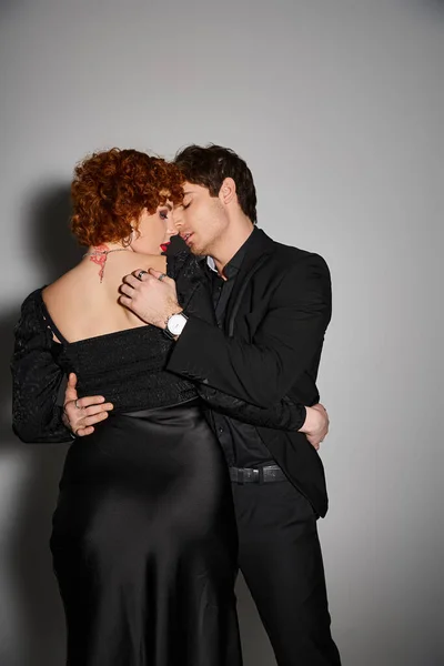 Alluring sexy couple in black elegant attires kissing and hugging lovingly on gray background — Stock Photo